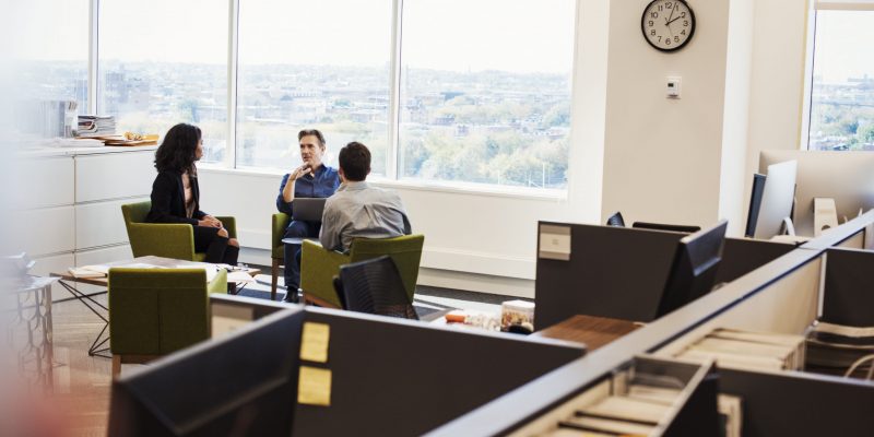 A woman and two men sitting in armchairs in an office talking to each other.