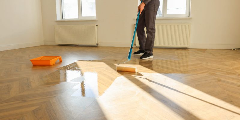 Man polishing parquet with varnish indoors, closeup